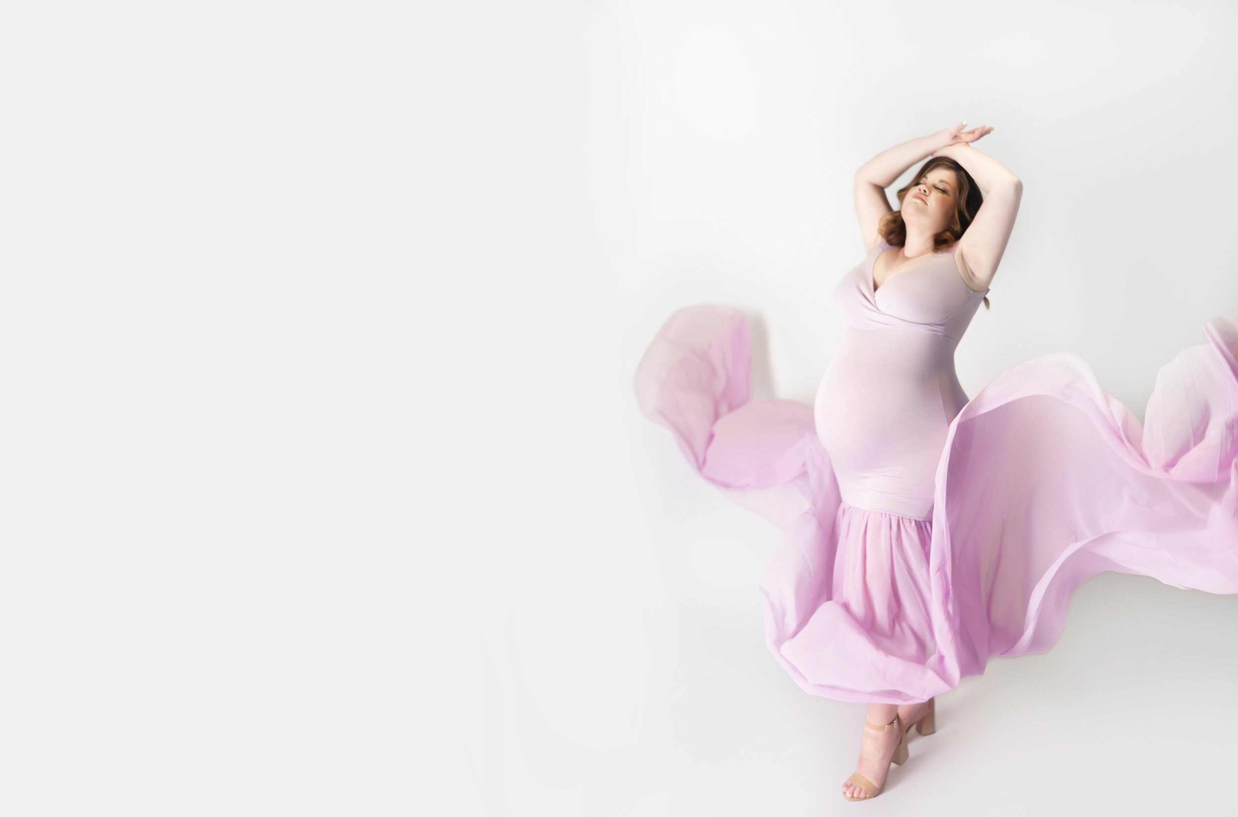 pregnant mom, wearing purple gown with arms above head, during maternity photoshoot in brentwood tennessee photography studio