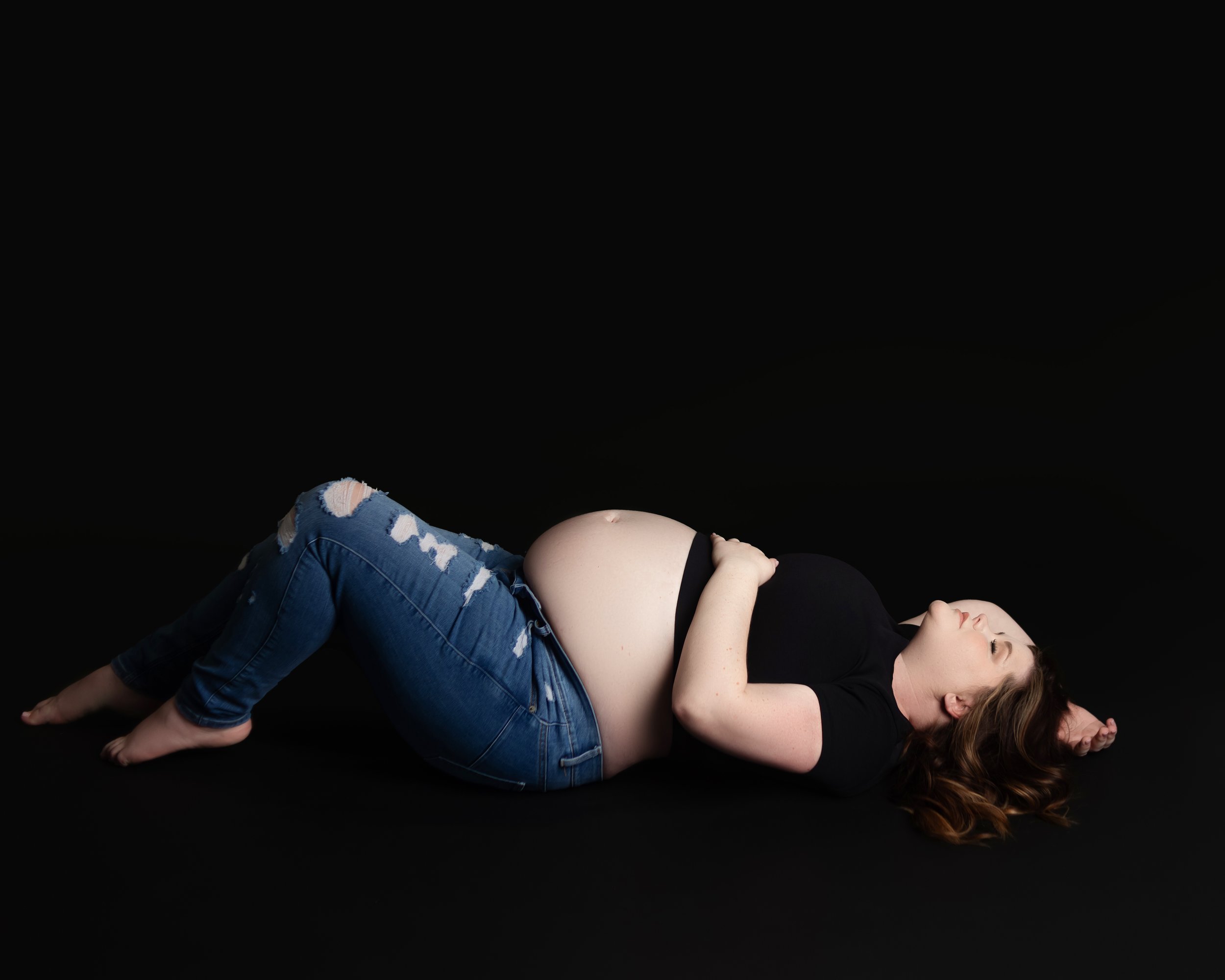 women laying on her back, holding her belly during maternity photoshoot in brentwood tennessee photograohy studio near me