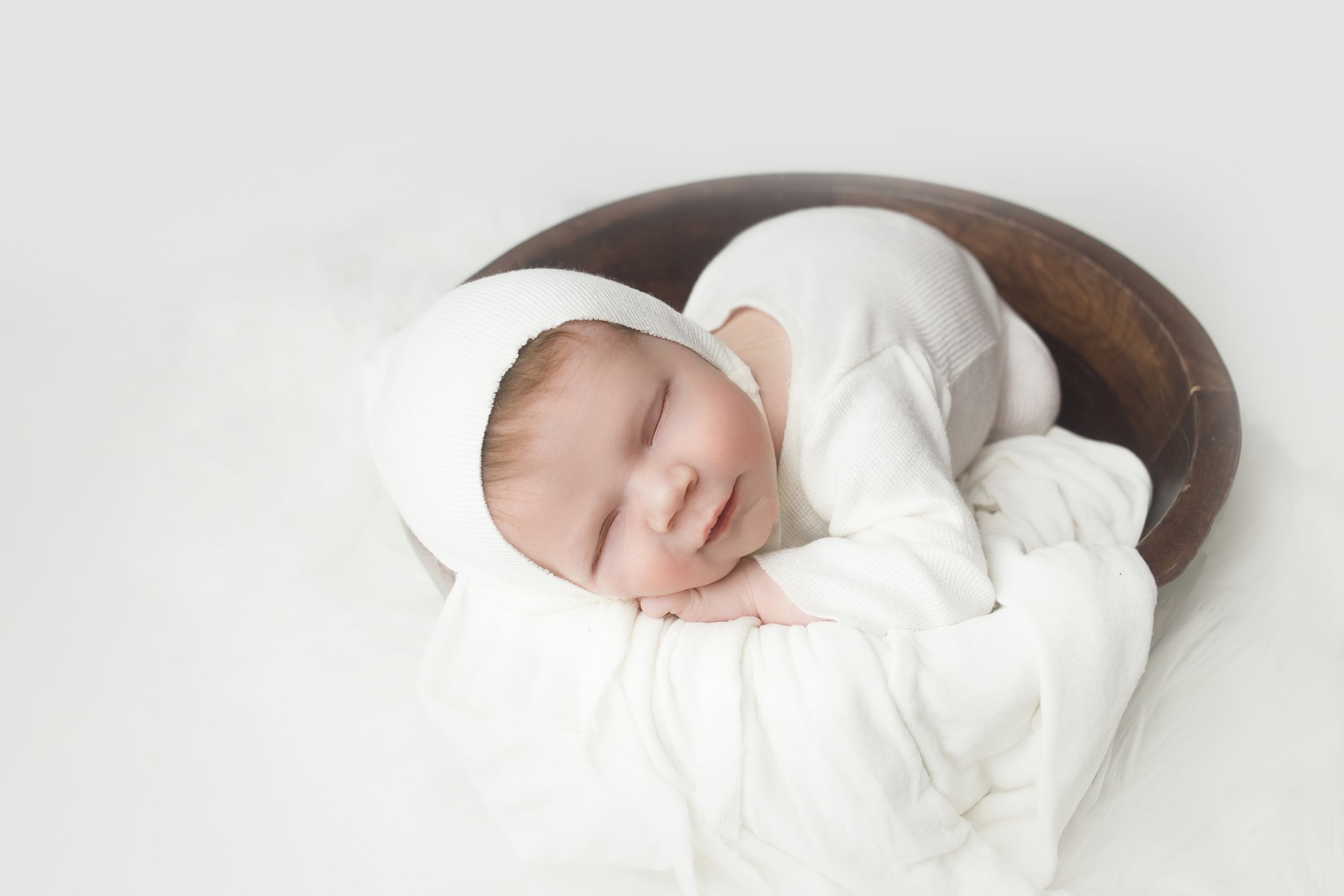 newborn boy, wearing white bonnet, sleeping in wood bowl during newborn photoshoot in mount juliet tennessee photography studio near me