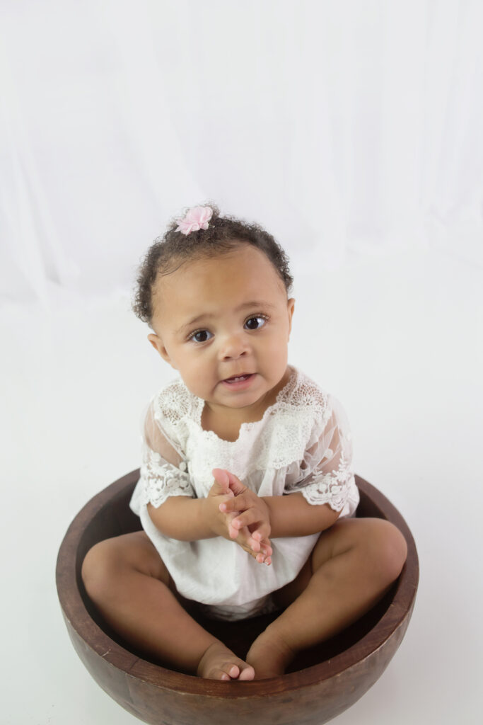 Little girl sitting in wood bowl during first birthday cake smash photoshoot in Franklin Tennessee photography studio 