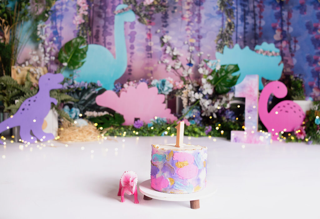 Pastel colored cake with dinosaur toy near it for cake smash photoshoot in Franklin Tennessee photography studio.