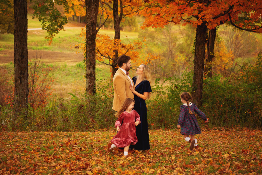 Girls running around their mother and father during fall mini session photoshoot with Mount Juliet, TN photographer in Nashville, Tennessee park 