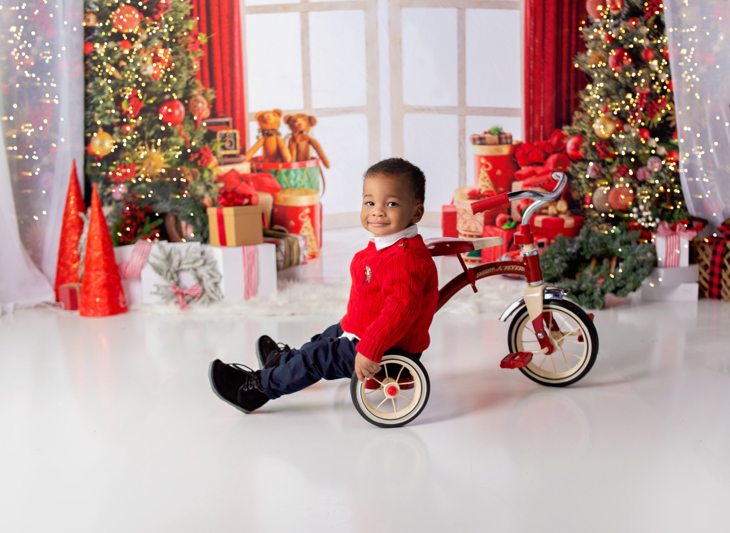 Little boy sitting on red tricycle during Christmas Mini session photoshoot